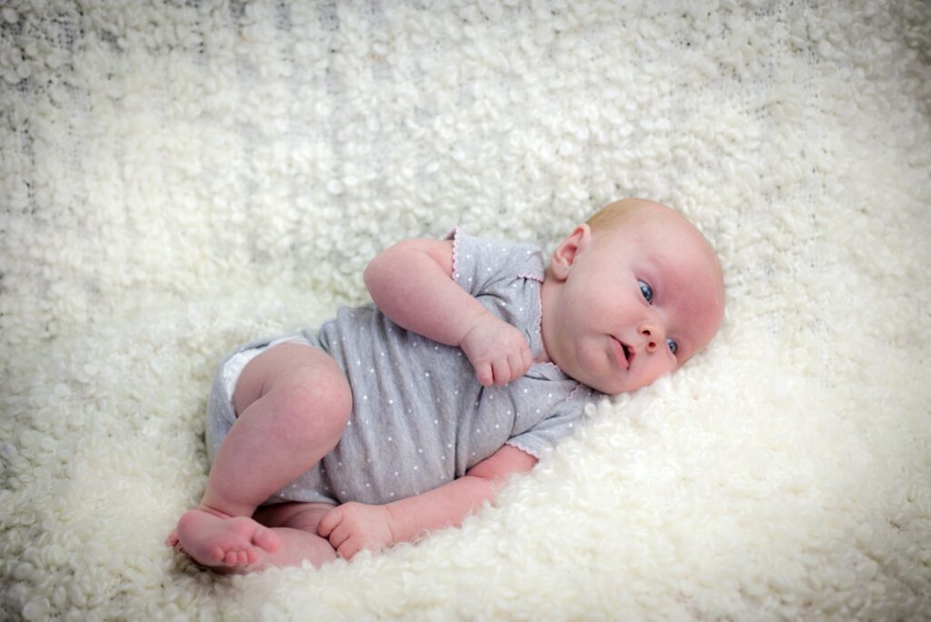 baby in gray onesie lying on white textile