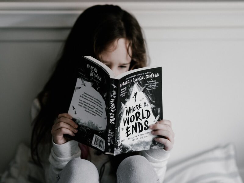 girl reading book on bed