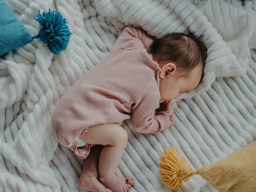 baby in pink onesie lying on white bed